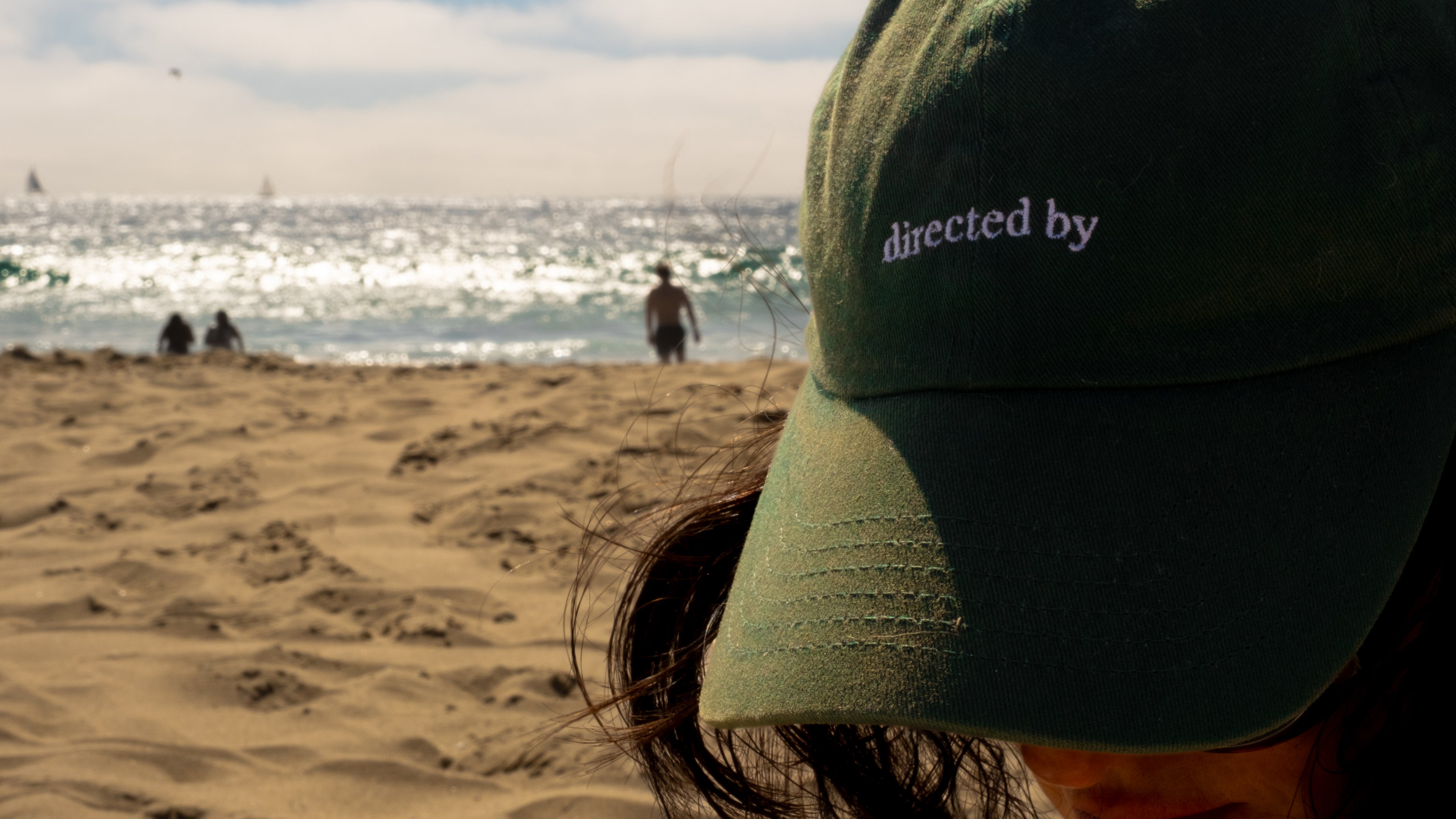 Person wearing a green cap with 'directed by' on a beach